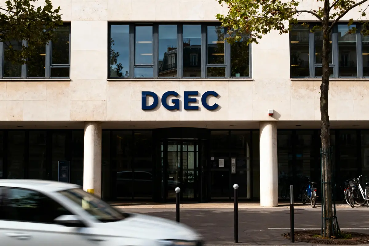 Façade d'un bâtiment avec logo "DGEC", voiture en mouvement, arbres et bicyclettes à l'extérieur.