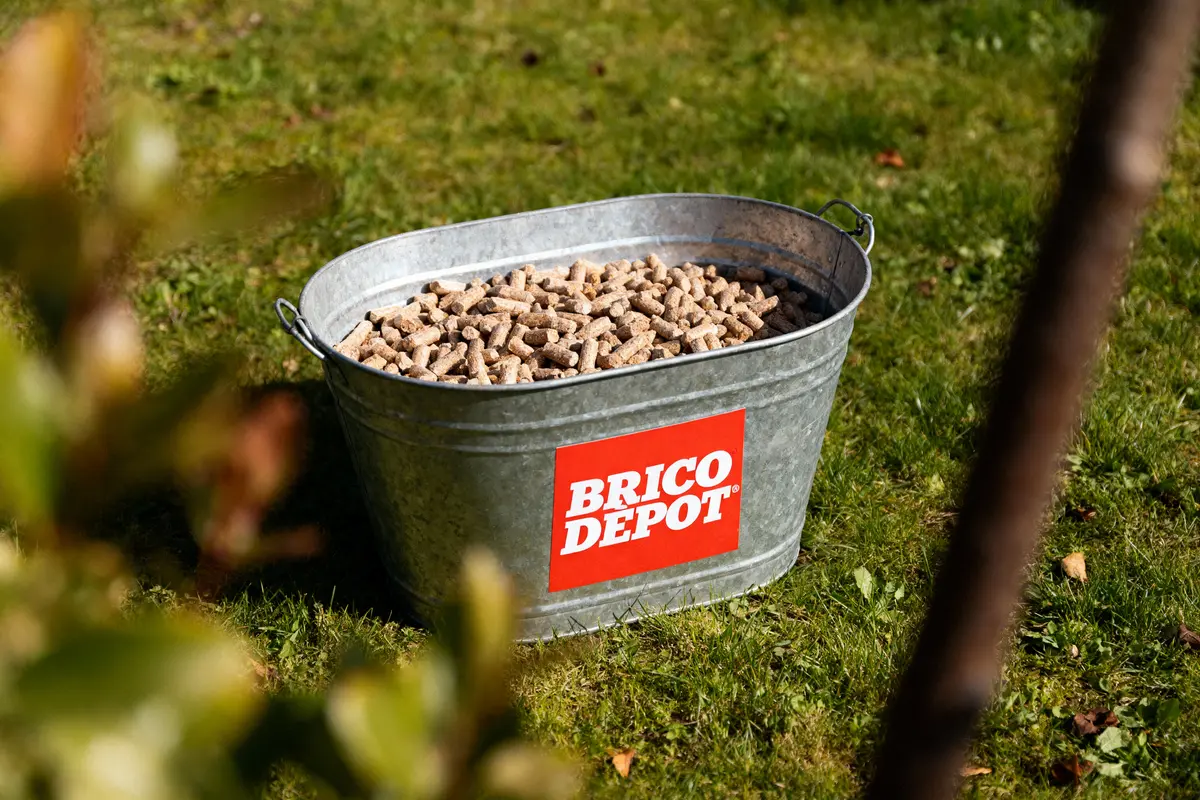 Seau métallique de granulés de bois sur herbe, marqué Brico Dépôt.