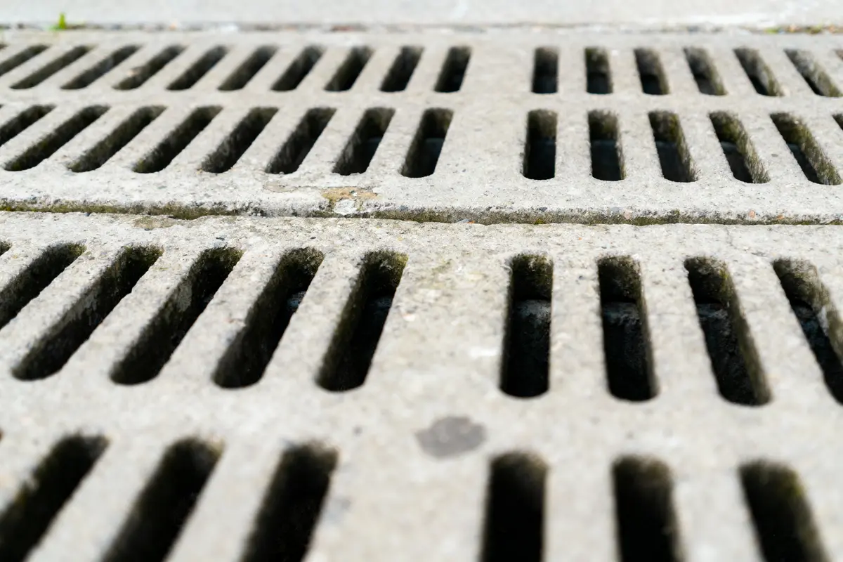 Grille d'égout en métal, gros plan, avec fentes parallèles et surface usée.