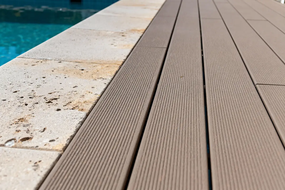 Plancher marron en bois composite près d'une piscine avec margelle en pierre claire.