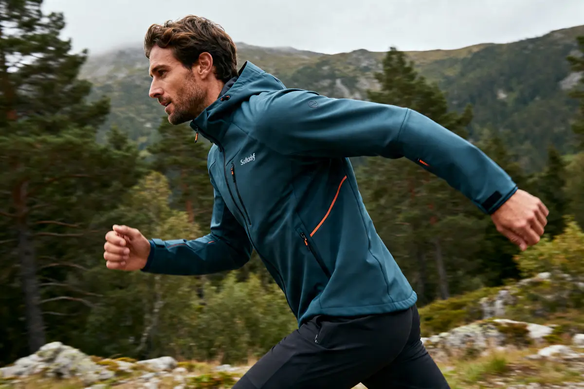 Homme courant en montagne portant une veste softshell Modyf bleu avec capuche en plein air
