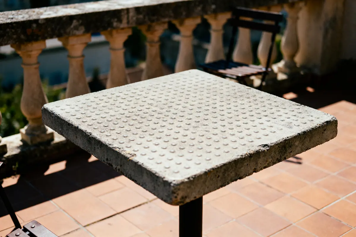 pexels-michal-pech-213601-757318 (1) Table carrée en pierre texturée, terrasse ensoleillée, balustrade en arrière-plan.